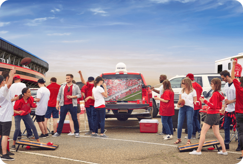 Group of people wearing red and white, tailgating with tv on the back of their truck.